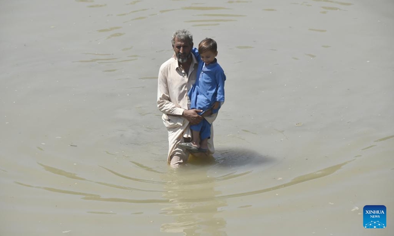 A man with a child wades through flooded water in northwest Pakistan's Charsadda on Aug. 31, 2022. The total death toll in Pakistan from this season's monsoon rains since mid-June has risen to at least 1,162, along with 3,554 others injured, the National Disaster Management Authority (NDMA) said.(Photo: Xinhua)