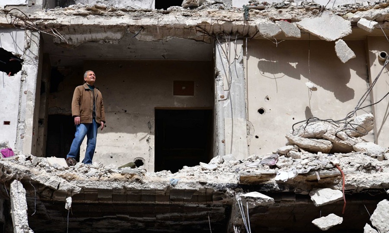 Hadi Ghusoun, a retired English teacher in his late 60s, stands on the porch of his shattered house in Homs city in central Syria, March 11, 2021.(Photo: Xinhua)