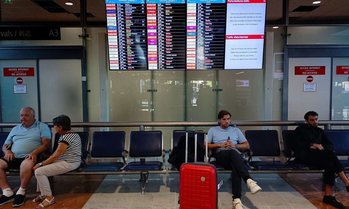 People sit next to a flight information board at Nice Cote d'Azur airport, in Nice, France on September 16, 2022. Over 1,000 flights were canceled due to a strike by air traffic controllers in France. Photo: IC