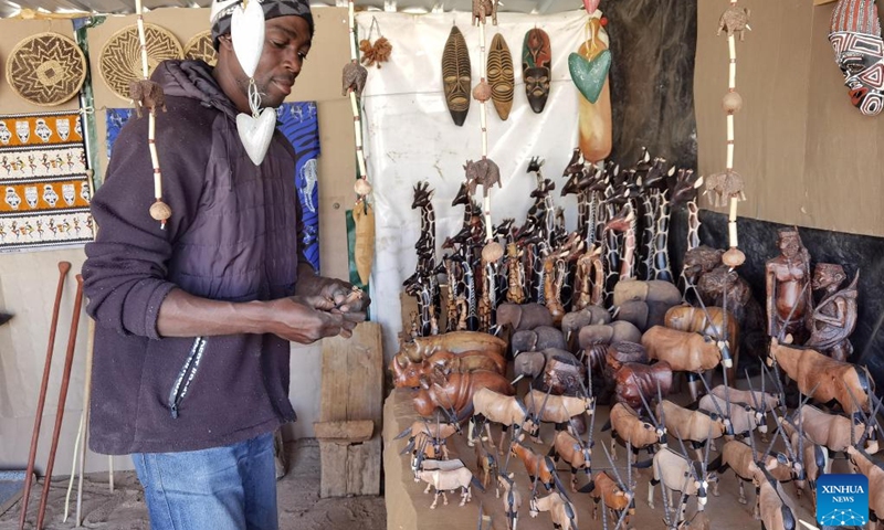 An artist arranges artwork at a market in Okahandja, Namibia, September 20, 2022. Namibian artists are maximizing the tradition of woodcarving to preserve cultural heritage and access larger markets from an open space on along the main road to Okahandja, a town 70 km north of Windhoek, the capital of Namibia.  (Photo: Xinhua)