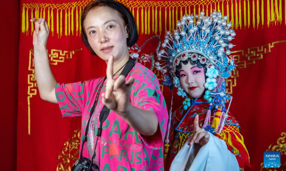 A child dressed in Chuanju (Sichuan opera) costume poses for photos under the guidance of a staff member in Ciqikou ancient town, southwest China's Chongqing Municipality, Oct. 2, 2022. During the National Day holiday, the scenic area Ciqikou has conducted various activities themed with traditional Chinese culture to attract tourists. (Xinhua/Tang Yi)