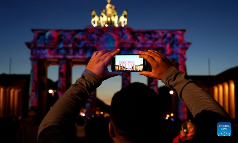 A visitor takes photos of the illuminated Brandenburg Gate during the 2022 Festival of Lights in Berlin, Germany, Oct. 7, 2022. (Photo by Stefan Zeitz/Xinhua)
