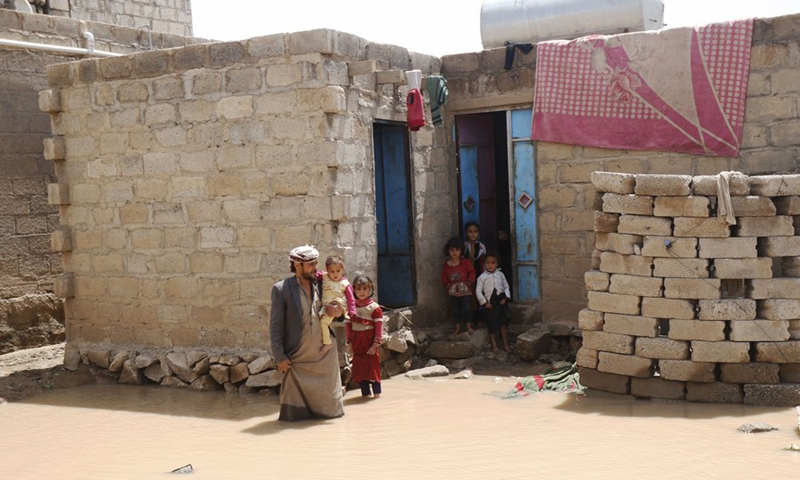 A man stands with his children outside their house surrounded by floods after heavy rains hit the Mabar District, Dhamar Province in Yemen on Aug. 23, 2022.(Photo: Xinhua)