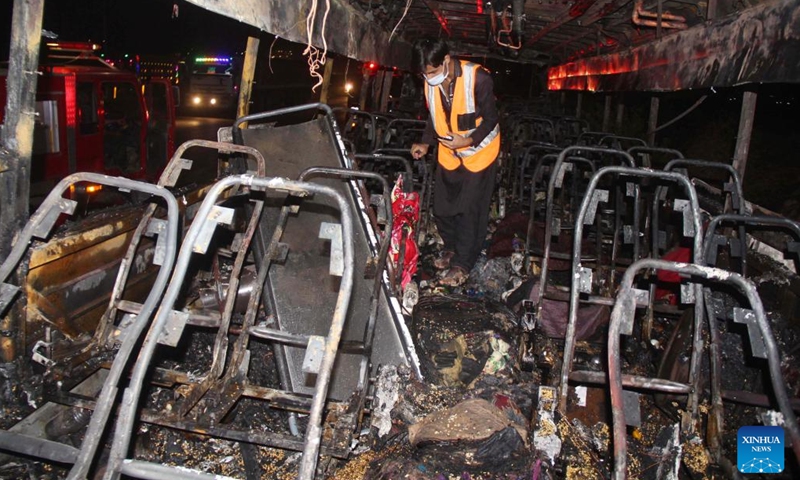 A rescuer examines a burnt passenger bus in Jamshoro district of Sindh province, Pakistan, Oct. 13, 2022. At least 18 people, including eight children, were killed and 28 others injured on Wednesday night after a passenger bus caught fire in Pakistan's southern Jamshoro district, police said on Thursday.(Photo: Xinhua)