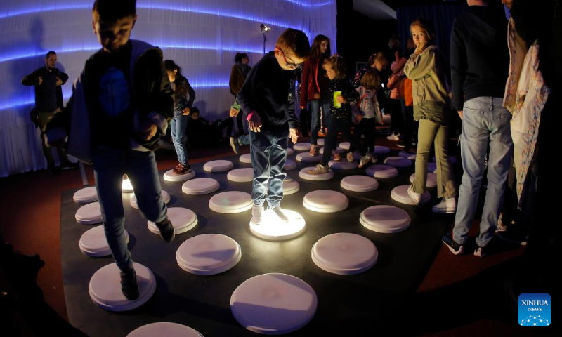 Children jump over a light installation while visiting the 3rd edition of the new media art festival RADAR in Bucharest, capital of Romania, Oct. 16, 2022. (Photo by Cristian Cristel/Xinhua)