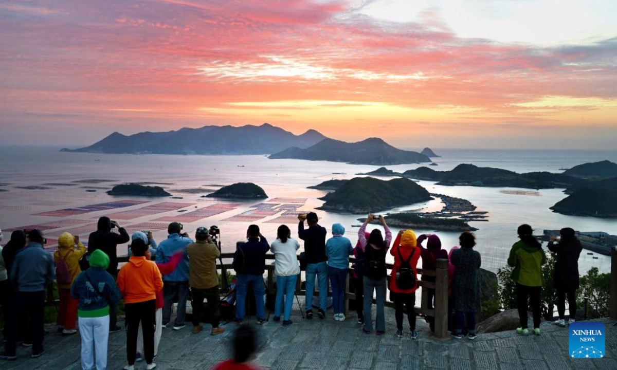 People take photos of the sunrise scenery by the seaside of Huazhu Village in Sansha Township, Xiapu County, southeast China's Fujian Province, Oct. 26, 2022. The sea area of Xiapu County has entered the peak season of autumn harvest. Boats travel through vast aquaculture area, harvesting aquatic products such as laver and oysters, from sunrise to sunset. Photo:Xinhua 