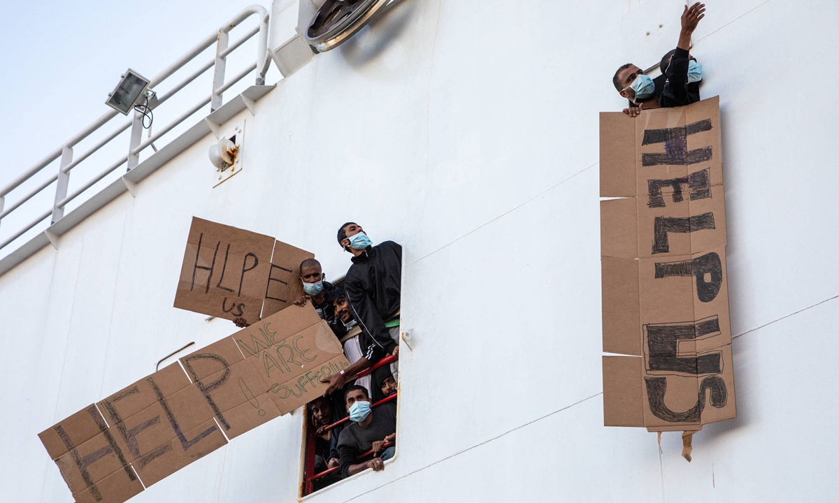 Migrants who have not been able to disembark wave signs with the words 