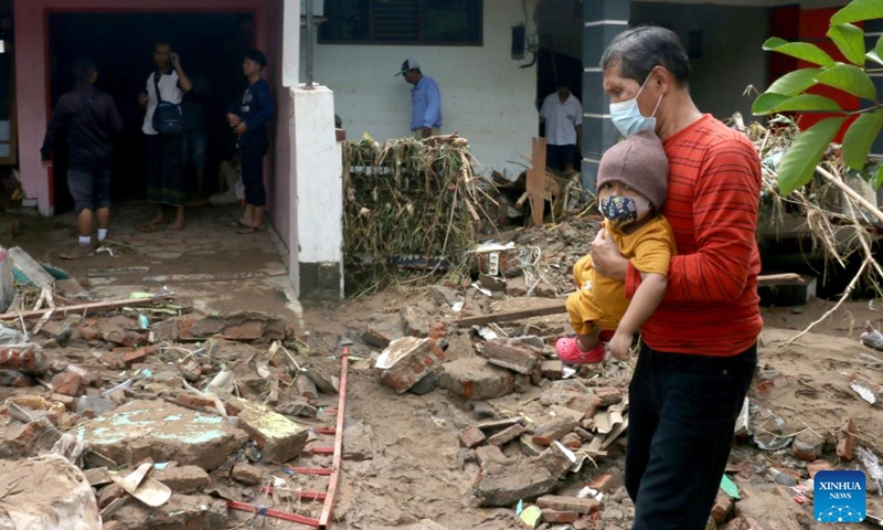 A man with a kid in his arms walks in front of damaged houses after flash flood hit at Wahyu Utomo Residence in Tambakaji, Semarang, Central Java, Indonesia, Nov. 7, 2022.(Photo: Xinhua)