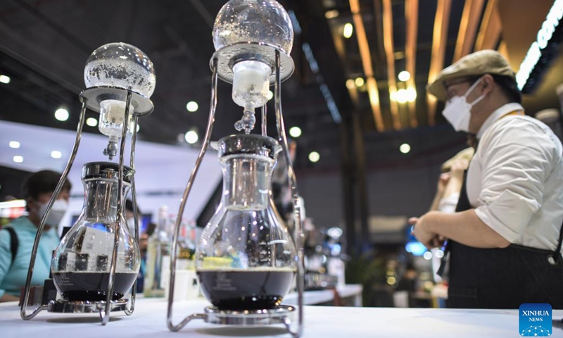 A staff member talks to visitors besides coffeepots during the fifth China International Import Expo (CIIE) in east China's Shanghai, Nov. 9, 2022. Various foods from around the world are showcased at the food and agricultural products exhibition area during the fifth CIIE in Shanghai.(Photo: Xinhua)