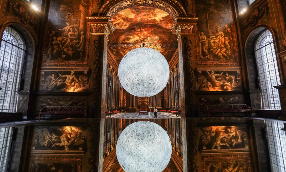 Luke Jerram’s Museum of the Moon is reflected in a glass table in the Painted Hall at the Old Royal Naval College in Greenwich, the UK, on December 12, 2022. Photo: VCG