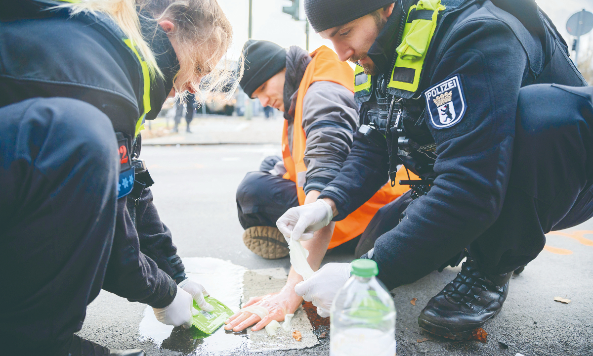 A climate activist (right) who taped his hand to a highway exit ramp at Innsbrucker Platz is cut loose by a police officer in Berlin, Germany on December 12, 2022. Photo: VCG