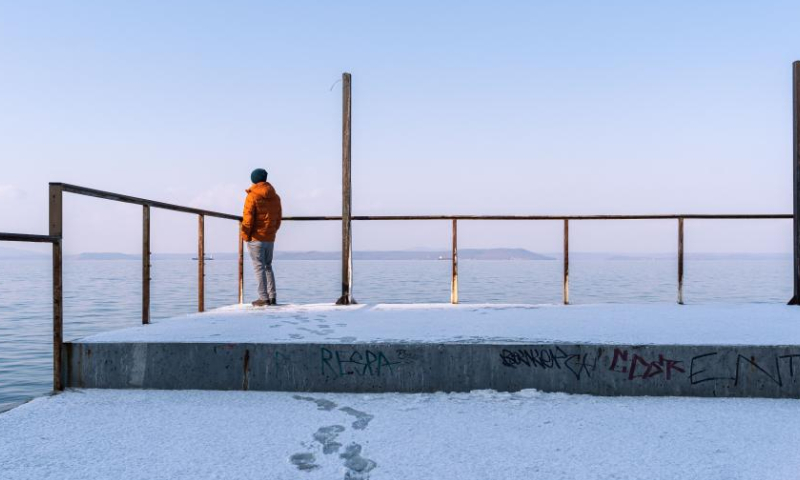 A man enjoys seaside view on a snow-covered pier in Vladivostok, Russia, Dec. 3, 2022. (Photo by Guo Feizhou/Xinhua)
