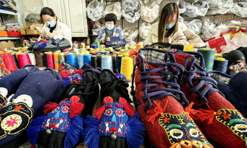 2022 年 12 月 1 日，中国东部山东省菏泽市，妇女们在一家工厂制作中国传统布鞋。（图片来源：中新社/高玉华）