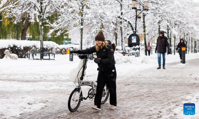 A woman pushes her bicycle on a snowy road in Stockholm, Sweden on Nov. 21, 2022. (Photo by Wei Xuechao/Xinhua)