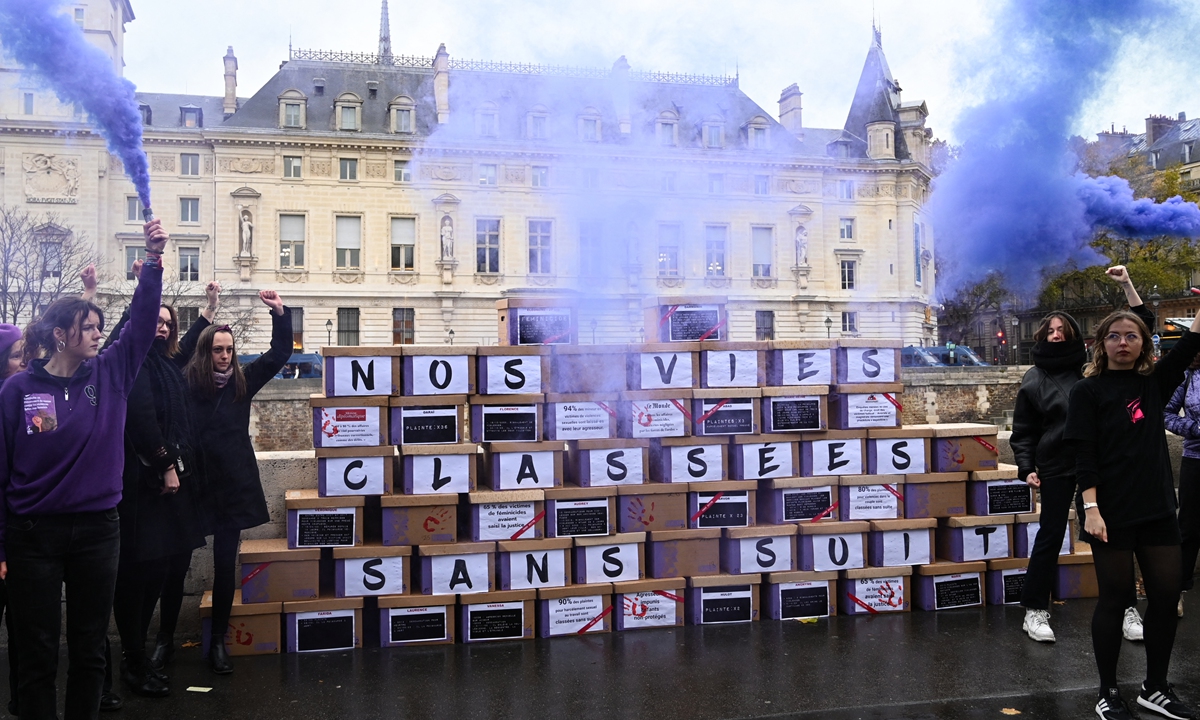 Demonstrators hold purple flare as they stand next to a wall made up of boxes of files with the inscription