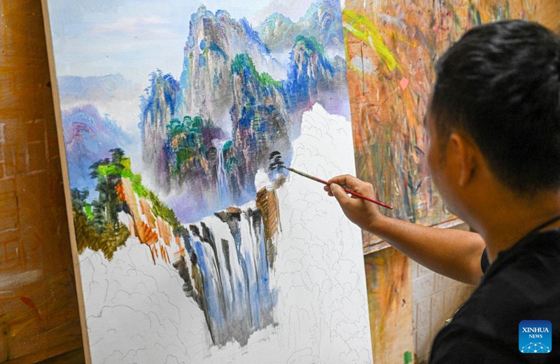 This photo taken on Nov 21, 2022 shows a painter painting an oil painting at a gallery on the oil painting street of Tunchang County, south China's Hainan Province. Tunchang County boasts oil painting as its characteristic industry. The annual production value of Tunchang oil paintings reaches about 7,000,000 RMB ($977,000). (Xinhua/Pu Xiaoxu)
