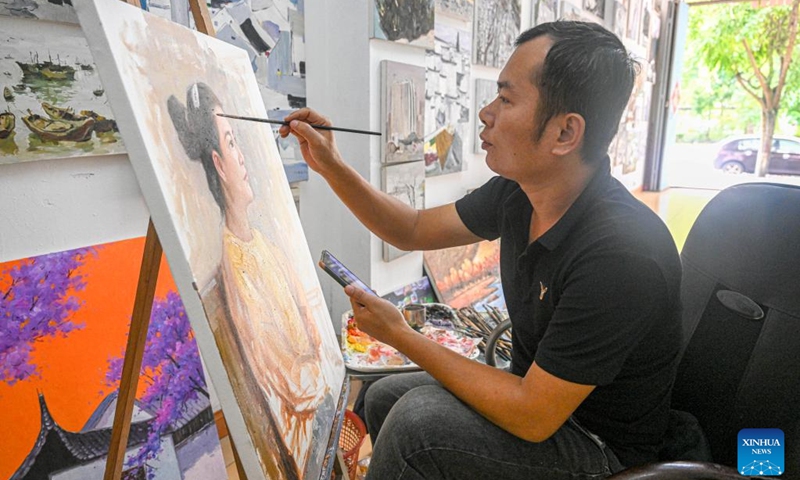 This photo taken on Nov 23, 2022 shows a painter painting an oil painting at a gallery on the oil painting street of Tunchang County, south China's Hainan Province. Tunchang County boasts oil painting as its characteristic industry. The annual production value of Tunchang oil paintings reaches about 7,000,000 RMB ($977,000). (Xinhua/Pu Xiaoxu)