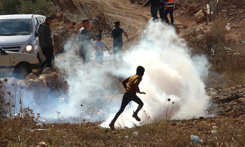 A protester runs to take cover from a tear gas canister fired by Israeli soldiers during clashes following a protest against the expansion of Jewish settlements in the West Bank village of Beit Dajan, east of Nablus, Nov. 11, 2022.(Photo: Xinhua)