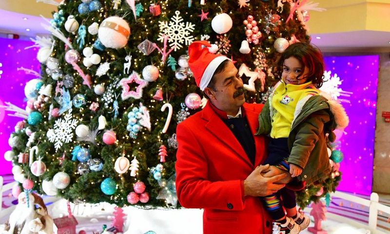 A man poses for a photo with his child near a Christmas tree in Damascus, Syria, Dec. 14, 2022.(Photo: Xinhua)