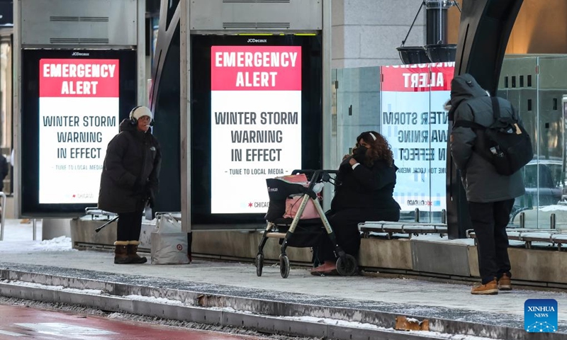 People wait for bus in Chicago, the United States, on Dec. 24, 2022. A strong winter storm swept through Chicago. (Photo by Joel Lerner/Xinhua)