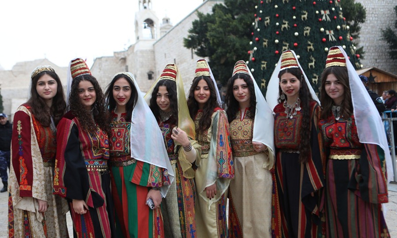 Women dressed in Palestinian traditional clothing pose for a picture during Christmas celebrations at the Manger Square in the West Bank city of Bethlehem on Dec. 24, 2022. (Photo by Mamoun Wazwaz/Xinhua)