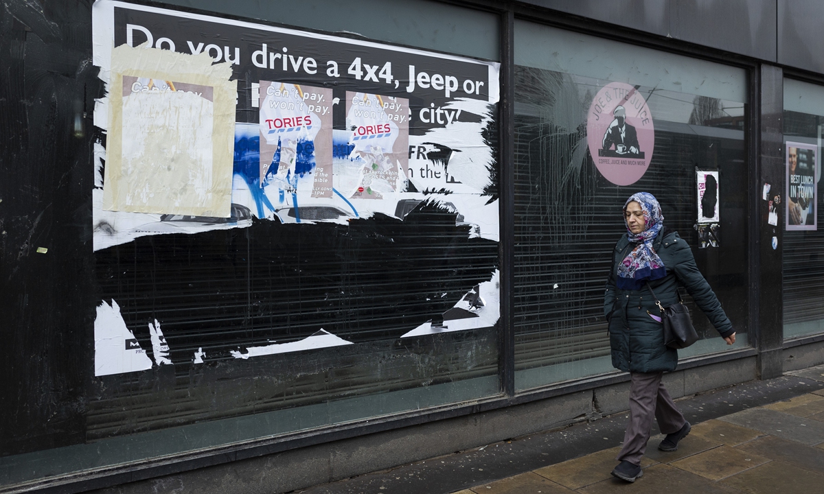 A woman passes torn protest posters in a vacant and neglected shop window on March 30, 2022 in Manchester, UK. Photo: VCG