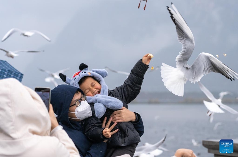 People feed black-headed gulls by the bank of Dianchi Lake in Kunming, southwest China's Yunnan Province, Jan. 1, 2023. People take part in various leisure activities to spend the New Year holiday. (Xinhua/Cao Mengyao)