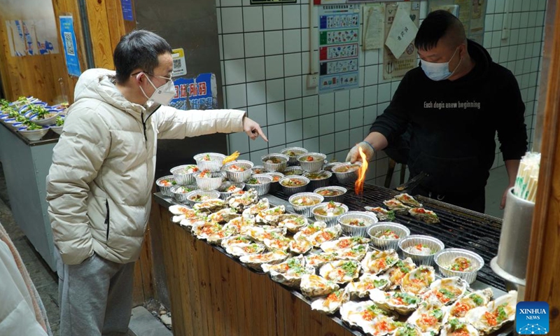 A man buys food on Furong Street in Jinan, east China's Shandong Province, Jan. 2, 2023. Furong Street, a 500-meter-long old street with more than 150 food and beverage shops, is getting back to its hustle and bustle these days.(Photo: Xinhua)