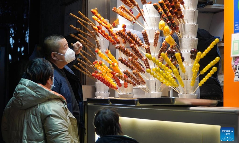 People buy sugar-coated haws on Furong Street in Jinan, east China's Shandong Province, Jan. 2, 2023. Furong Street, a 500-meter-long old street with more than 150 food and beverage shops, is getting back to its hustle and bustle these days.(Photo: Xinhua)