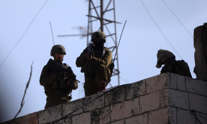 An Israeli soldier aims his weapon at Palestinian protesters during clashes in the West Bank city of Hebron, on Jan. 26, 2023. Israeli forces killed on Thursday at least nine Palestinians, including an elderly woman, during a raid in the occupied West Bank, Palestinian sources said, amid escalating violence in the region. Photo: Xinhua