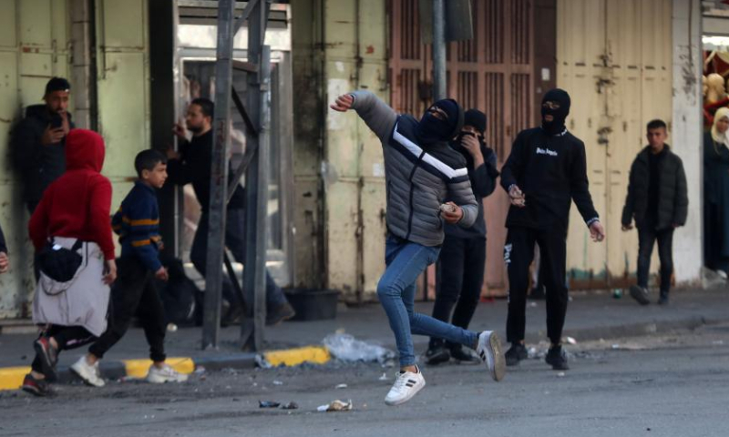 A Palestinian protester hurls a stone at Israeli soldiers during clashes in the West Bank city of Hebron, on Jan. 26, 2023. Israeli forces killed on Thursday at least nine Palestinians, including an elderly woman, during a raid in the occupied West Bank, Palestinian sources said, amid escalating violence in the region. Photo: Xinhua