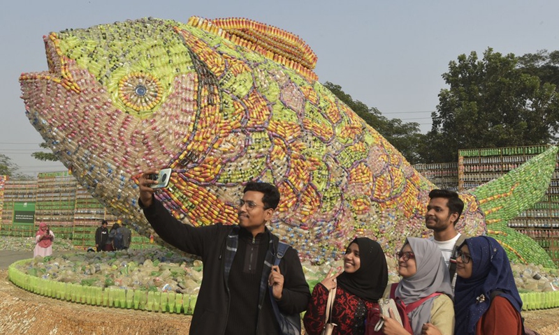 People take selfies in front of a fish-shaped installation made of empty plastic bottles and cigarette filters at an exhibition in Bangladeshi capital Dhaka, Jan. 5, 2023. (Photo by Salim/Xinhua) 