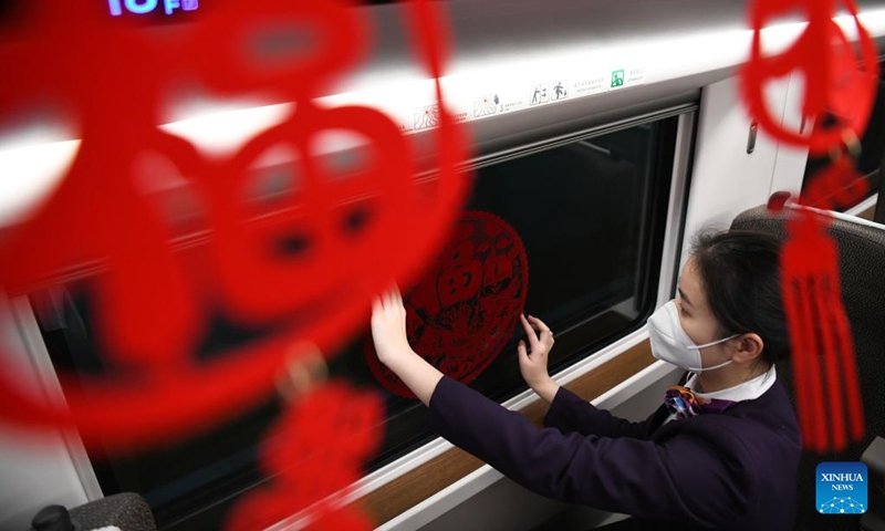 Wang Hao, crew member of train No.G9480, decorates a train car with Spring Festival ornaments before the train leaves Bozhou South Railway Station in Bozhou, east China's Anhui Province, Jan. 13, 2023. The Hefei branch of China Railway Shanghai Bureau Group Co., Ltd. has added temporary night trains to meet the needs of travellers during the Spring Festival travel rush. (Xinhua/Zhang Duan)