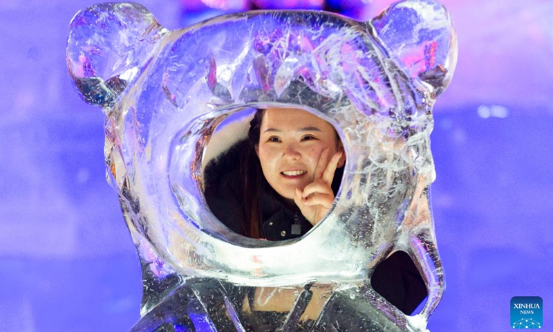 A tourist poses for photos with an ice sculpture in Harbin, northeast China's Heilongjiang Province, Jan. 14, 2023. Harbin is famous for its rich ice and snow resources. This winter, the city opened three ice and snow-themed parks, launched 12 ice and snow experience products and 10 such tourism routes, and created more than 100 related activities to promote the development of winter tourism, culture, fashion and sports. (Xinhua/Xie Jianfei)