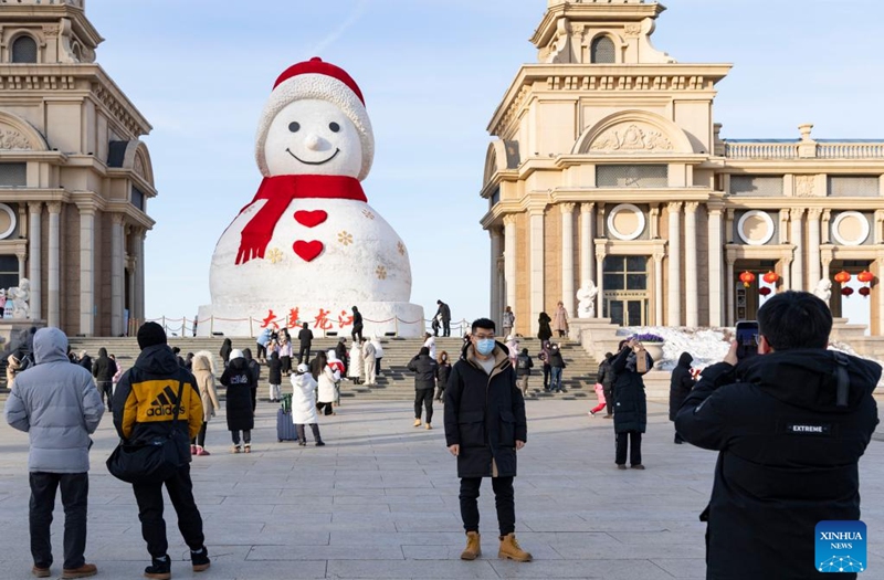 People pose for photos with a giant snowman in Harbin, northeast China's Heilongjiang Province, Jan. 14, 2023. Harbin is famous for its rich ice and snow resources. This winter, the city opened three ice and snow-themed parks, launched 12 ice and snow experience products and 10 such tourism routes, and created more than 100 related activities to promote the development of winter tourism, culture, fashion and sports. (Xinhua/Xie Jianfei)