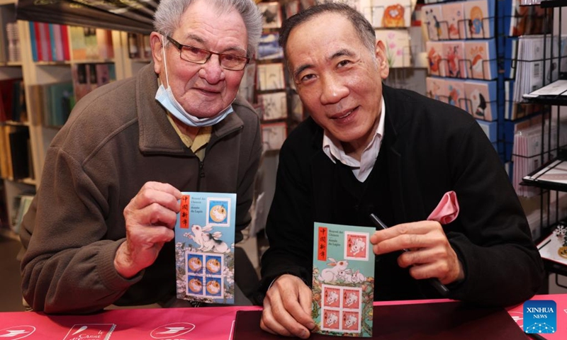 A customer poses for a photo with Chinese artist Chen Jianghong (R), designer of the Year of the Rabbit commemorative stamps, during a launching ceremony in Paris, France, Jan. 14, 2023. (Xinhua/Gao Jing)