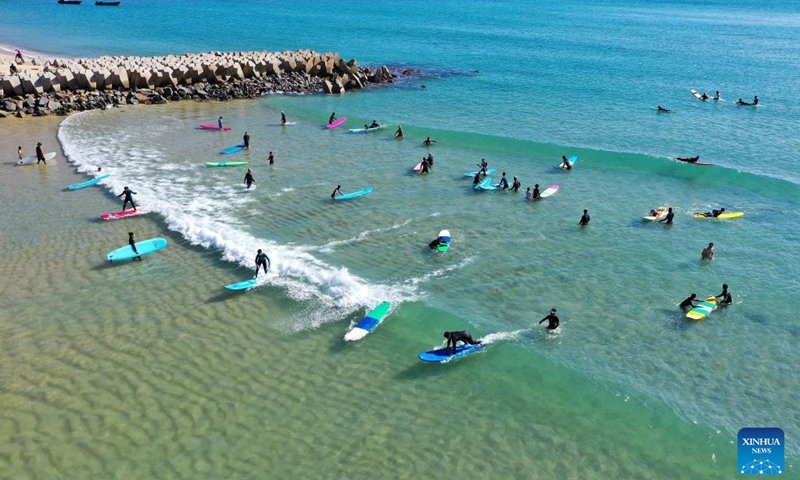 This aerial photo shows tourists going surfing at Riyue Bay in Wanning, south China's Hainan Province, Jan. 14, 2023. Surfing has become a symbol of Wanning thanks to its unique geographical and climatic advantages. (Xinhua/Guo Cheng)