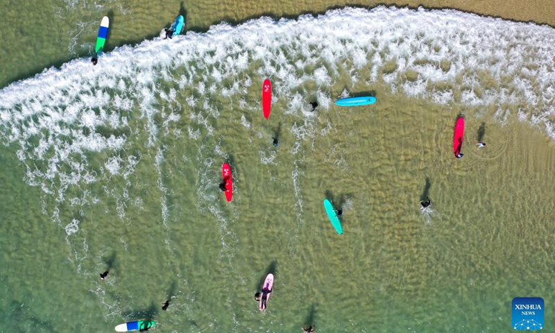 This aerial photo shows tourists going surfing at Riyue Bay in Wanning, south China's Hainan Province, Jan. 14, 2023. Surfing has become a symbol of Wanning thanks to its unique geographical and climatic advantages. (Xinhua/Guo Cheng)