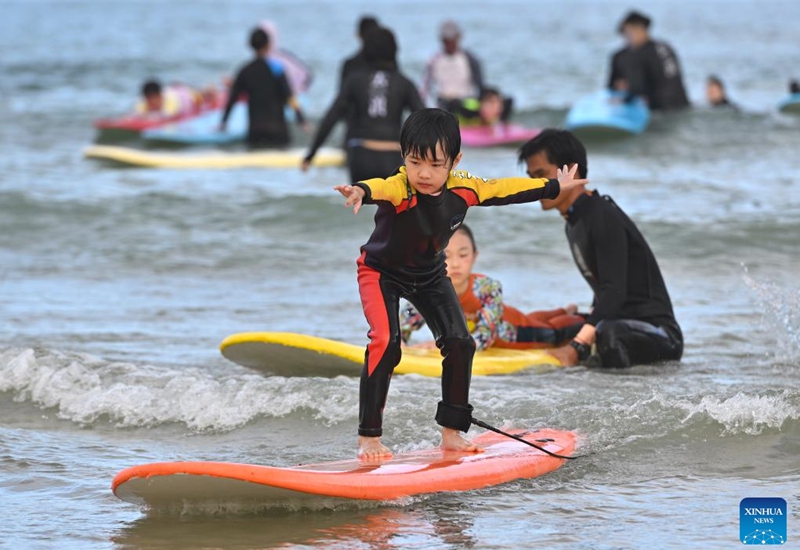 A child goes surfing at Riyue Bay in Wanning, south China's Hainan Province, Jan. 13, 2023. Surfing has become a symbol of Wanning thanks to its unique geographical and climatic advantages. (Xinhua/Guo Cheng)