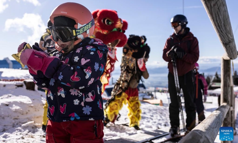 A child gets a lucky bag presented by lion dance performers at the Krvavec Ski Resort in Slovenia, Jan. 14, 2023.(Photo by Zeljko Stevanic/Xinhua)