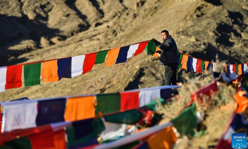 A man hangs prayer flags on a mountain in Xigaze, southwest China's Tibet Autonomous Region, Jan. 24, 2023. Following the tradition, people here went early in the morning to hang new prayer flags on top of mountains and their house roofs to celebrate New Year under the Tibetan calendar. (Xinhua/Jigme Dorje)