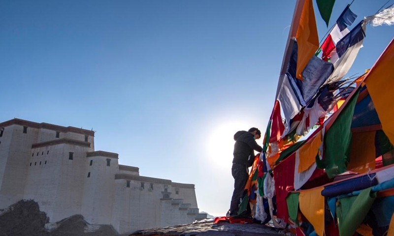 A man hangs prayer flags in Xigaze, southwest China's Tibet Autonomous Region, Jan. 24, 2023. Following the tradition, people here went early in the morning to hang new prayer flags on top of mountains and their house roofs to celebrate New Year under the Tibetan calendar. (Xinhua/Sun Fei)