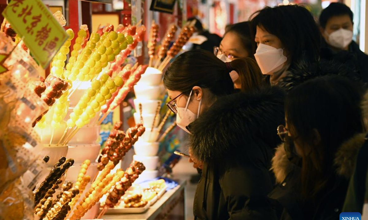 People buy Tanghulu, a traditional Chinese snack of candied fruit, in Beijing, capital of China, Jan. 23, 2023. People enjoy various kinds of cuisine in China during the Spring Festival holiday. (Xinhua/Ren Chao)



