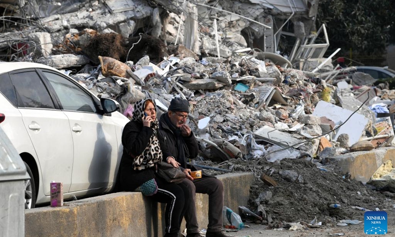 People sit beside earthquake debris in Antakya, Hatay province, Türkiye, on Feb. 11, 2023. The death toll from Monday's devastating earthquakes climbed to 22,327 in Türkiye, while another 80,278 injuries were reported in the country, Turkish Health Minister Fahrettin Koca announced on Saturday night.(Photo: Xinhua)