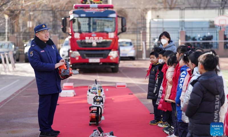 A firefighter (1st L) introduces firefighting equipment to students at a primary school on the first day of the new semester in Beijing, capital of China, Feb. 13, 2023. Primary and middle school students in Beijing returned to school for the spring semester on Monday.(Photo: Xinhua)
