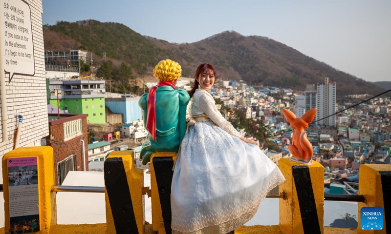 A tourist poses for a photo with a Little Prince sculpture at Gamcheon Culture Village in Busan, South Korea, March 7, 2023. Located on the foothills of a coastal mountain in Busan, Gamcheon Culture Village is famous for houses built in staircase-fashion and alleys decorated with wall paintings and sculptures.(Photo: Xinhua)