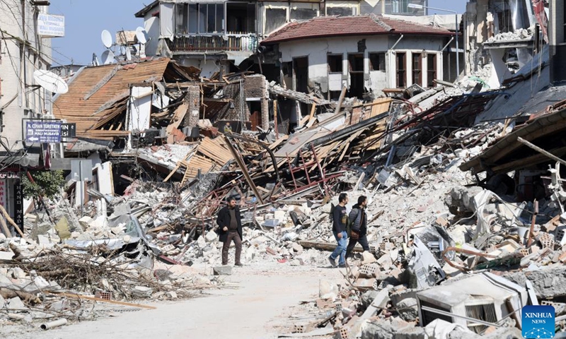People walk past a collapsed building in the quake-hit city of Antakya, Türkiye, on March 7, 2023.(Photo: Xinhua)