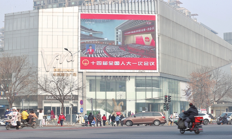 Passengers watch a large outdoor screen that broadcasts the first session of the 14th National People's Congress (NPC) in Beijing on March 5, 2023. The first session of the 14th NPC kicked off at the Great Hall of the People on the same day. Photo:cnsphoto