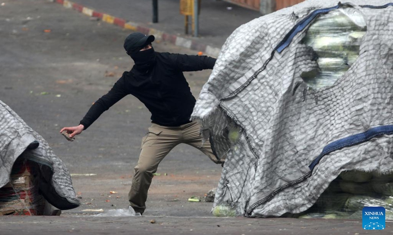 A Palestinian protester throws a stone at Israeli security forces during clashes following a protest over the killing of six Palestinians, in the West Bank city of Hebron, on March 8, 2023. Outrage and grief prevailed in the Palestinian territories on Wednesday, a day after six Palestinians were killed and 26 others injured during an Israeli raid near the West Bank city of Jenin.(Photo: Xinhua)
