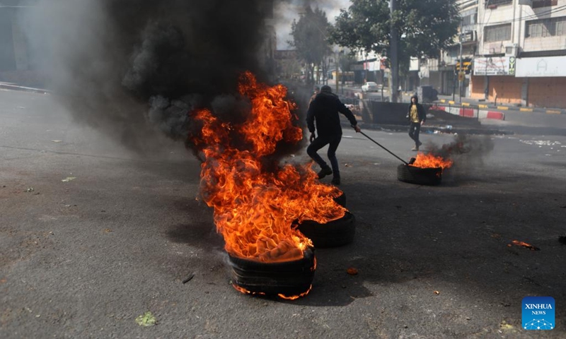 A Palestinian protester pulls a burning tire during clashes with Israeli security forces following a protest over the killing of six Palestinians, in the West Bank city of Hebron, on March 8, 2023. Outrage and grief prevailed in the Palestinian territories on Wednesday, a day after six Palestinians were killed and 26 others injured during an Israeli raid near the West Bank city of Jenin.(Photo: Xinhua)